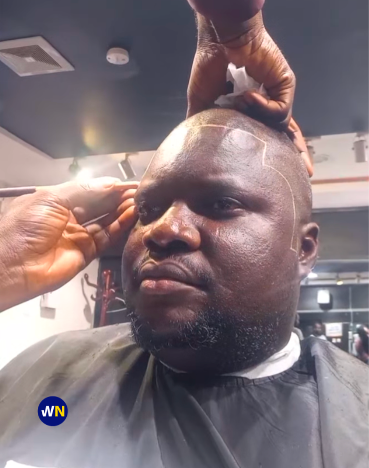 A close-up shot of a man receiving a precise hairline trim from a barber in a modern, well-lit barbershop in Wuse, Abuja. The man has a focused expression, and the clean lines of his cut are clearly visible.