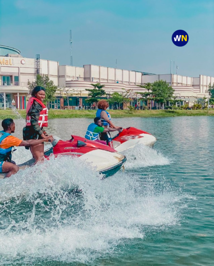 People wearing life jackets riding jet skis across Jabi Lake with Jabi Lake Mall visible in the background.